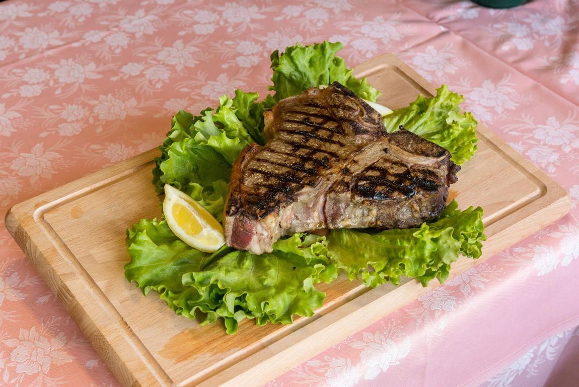 Primo piano di una bistecca con il centro rosato su una crosta scura, adagiata su un letto di verdure su uno sfondo scuro.