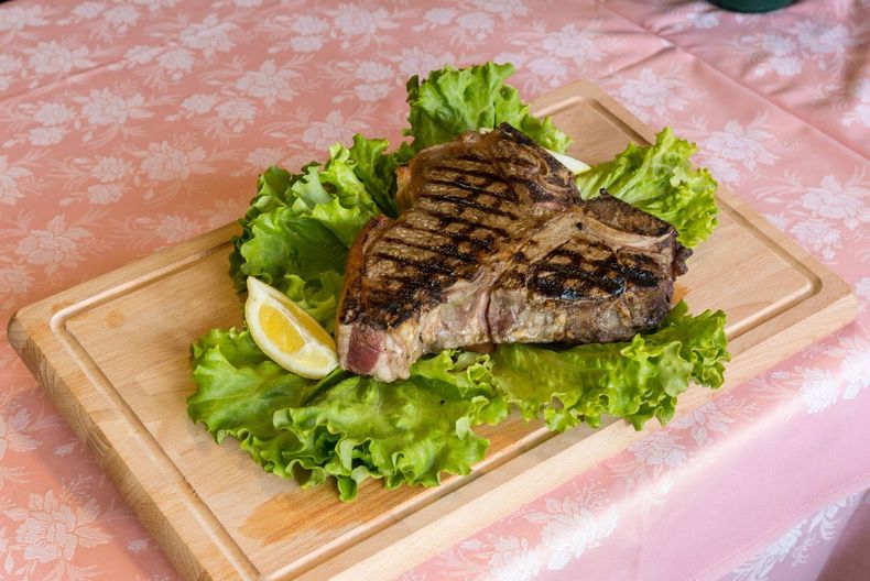 Primo piano di una bistecca rosa scottata con una crosticina dorata su un letto di erbe aromatiche.