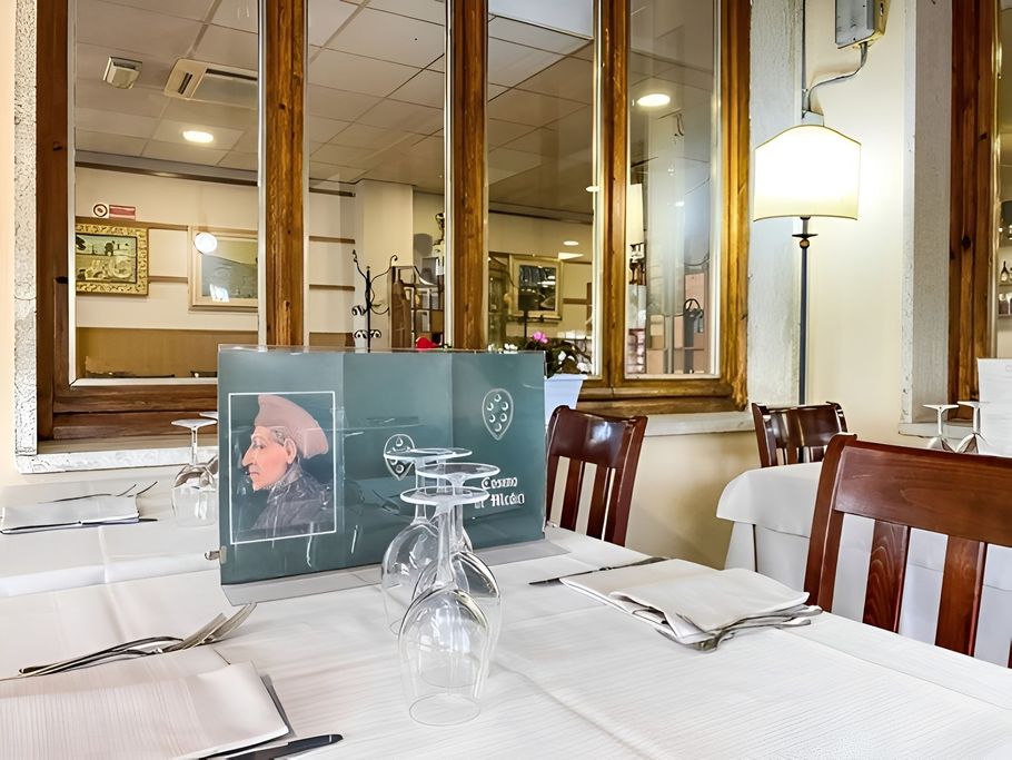 In un luminoso interno di ristorante, il tavolo da pranzo è apparecchiato con tovaglie bianche, bicchieri, menù e sedie in legno.