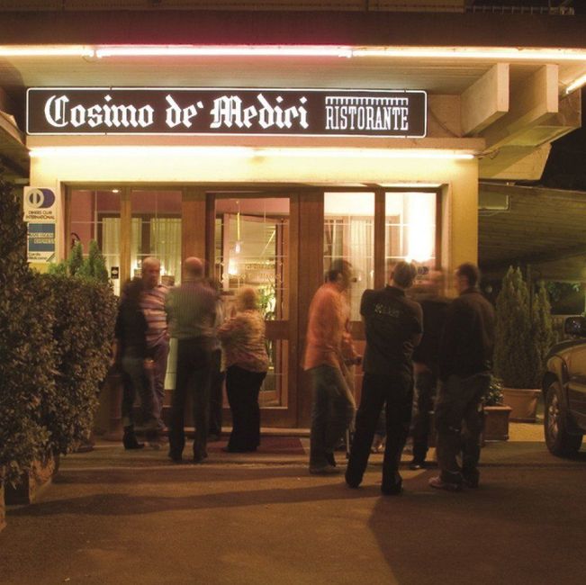 Di sera, alcune persone si sono radunate fuori dal ristorante Cosimo de' Medici, sotto un'insegna luminosa.