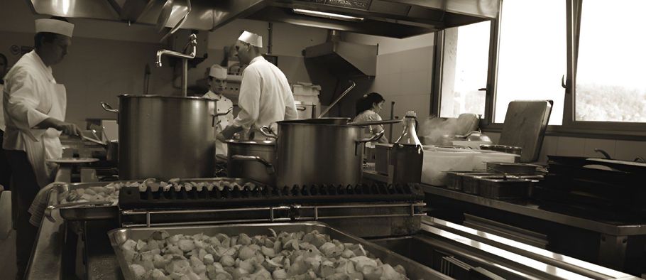 Operai che preparano il cibo in una cucina commerciale, accanto a vassoi di pasta o ravioli.