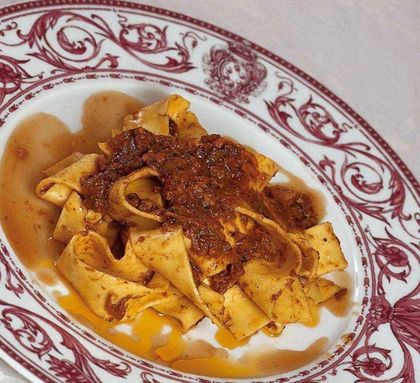 Pasta al ragù su un piatto bianco con bordo decorativo rosso.