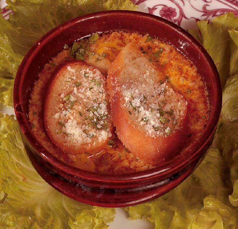 Una ciotola di pasta al forno con formaggio ed erbe aromatiche, servita su un piatto foderato di lattuga.