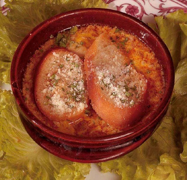 Zuppa in una ciotola rossa, guarnita con crostini e formaggio grattugiato su foglie di lattuga.