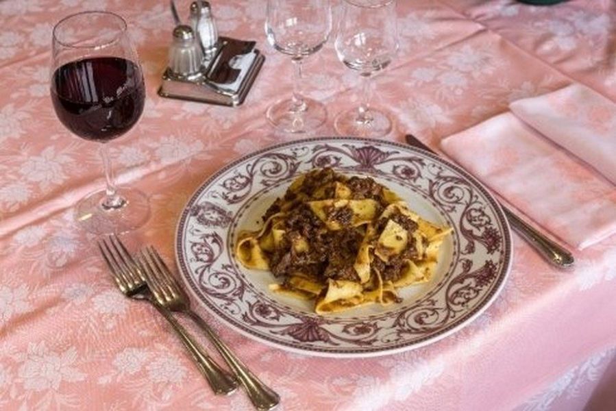 Pasta su un piatto decorato con un bicchiere di vino rosso su una tovaglia rosa, apparecchiata per un pasto
