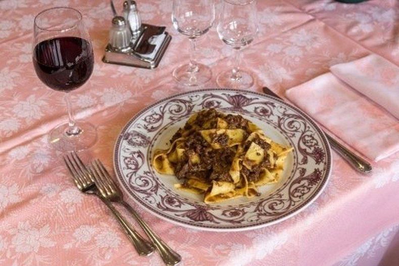 Mani che stendono la pasta fresca su un piano di lavoro infarinato in cucina.