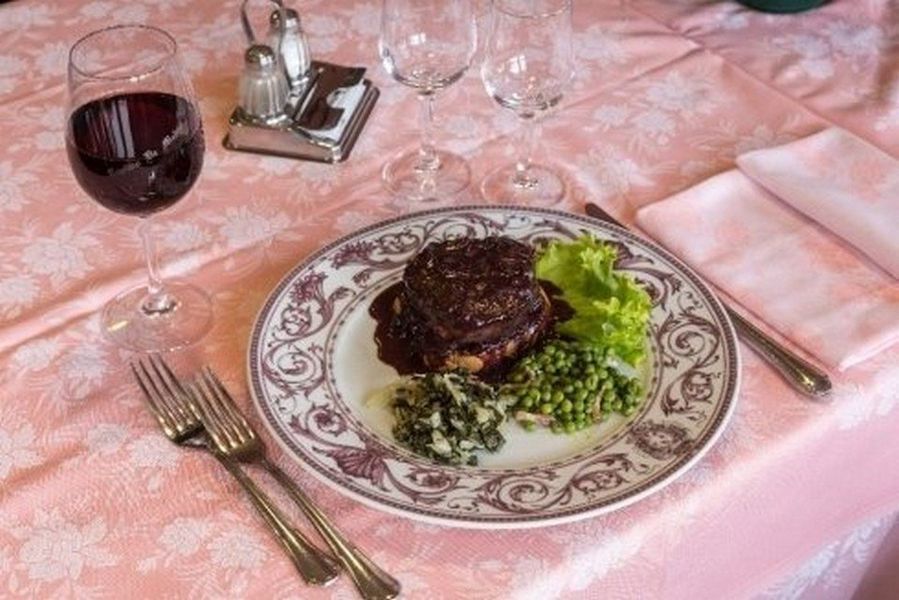 Elegante apparecchiatura della tavola con bistecca, verdure e un bicchiere di vino rosso su una tovaglia rosa.