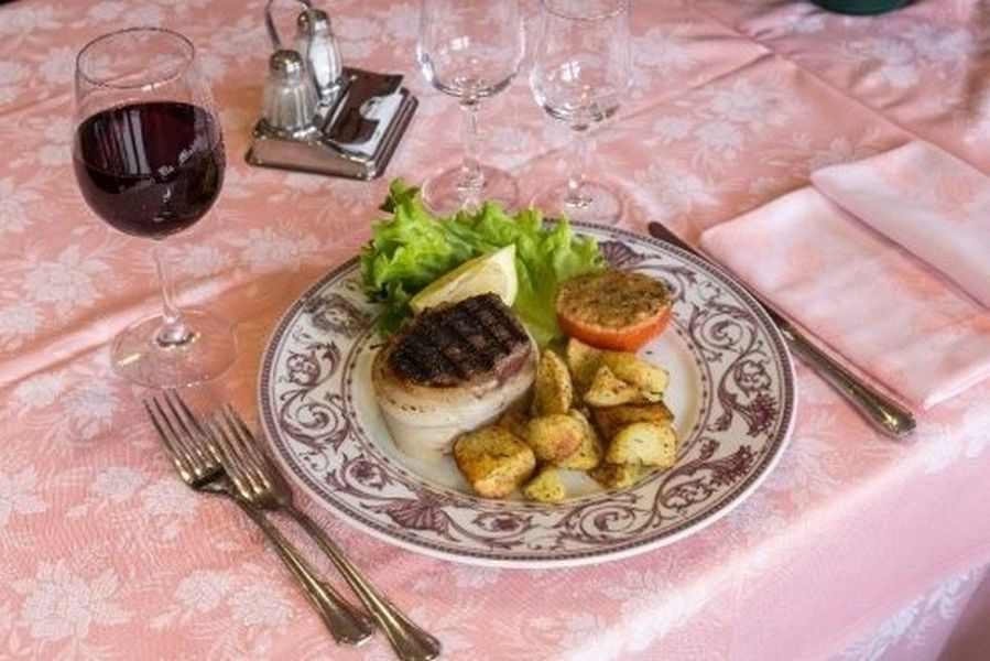 Piatto gourmet servito con calice da vino e posate su una tovaglia rosa.