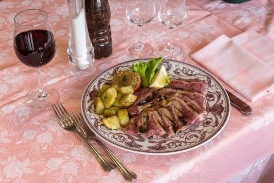 Tavola apparecchiata con affettati, patate, vino e tovaglia rosa su un piatto decorato.