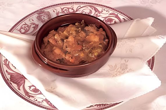 Una piccola ciotola di cibo su un piatto decorativo con tovaglioli bianchi piegati.