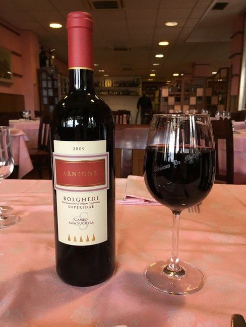 Una bottiglia di vino e un bicchiere pieno su un tavolo di ristorante con una tovaglia rosa.