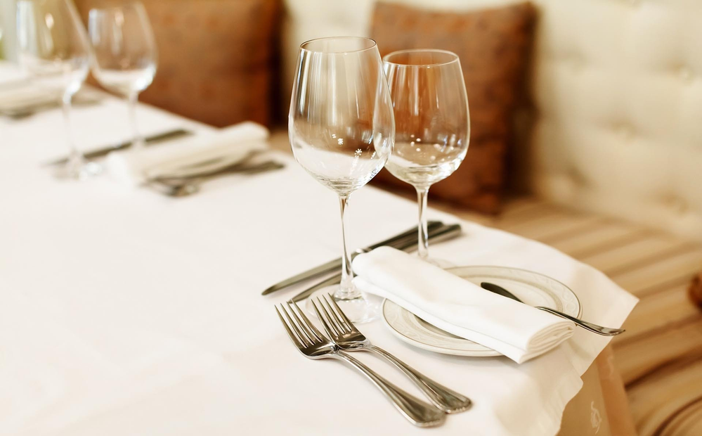 Apparecchiare la tavola con bicchieri da vino, tovaglioli piegati e posate in un'atmosfera accogliente da ristorante.