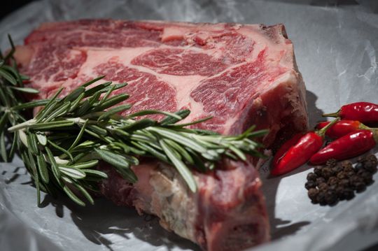 Bistecca di manzo cruda marmorizzata con rosmarino, peperoncini rossi e grani di pepe su carta da forno.