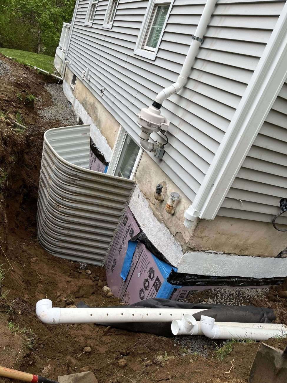Foundation drainage system near completion with PVC discharge lines and gravel backfill
