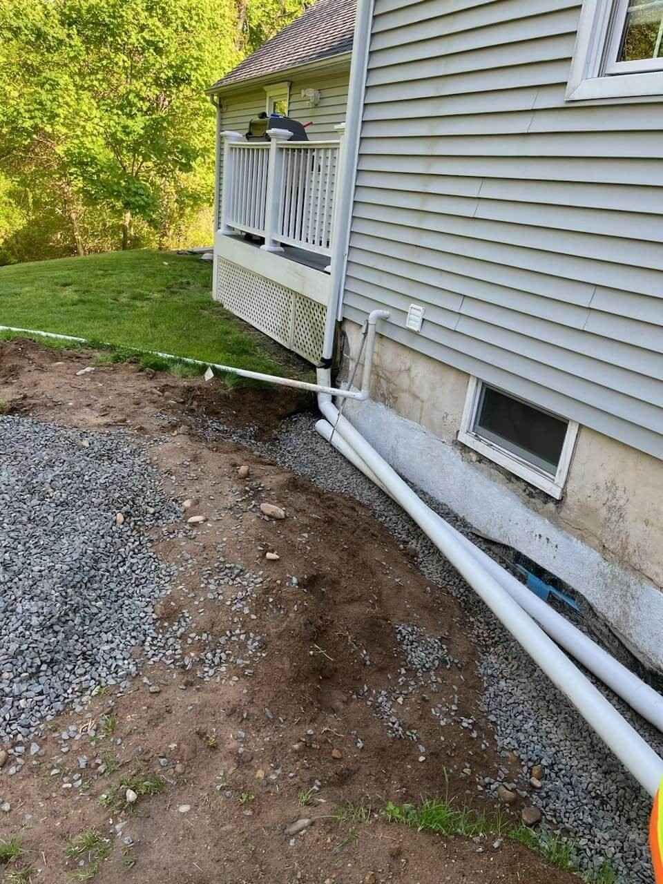 Foundation excavation showing waterproofing membrane, foam insulation, and downspout connection