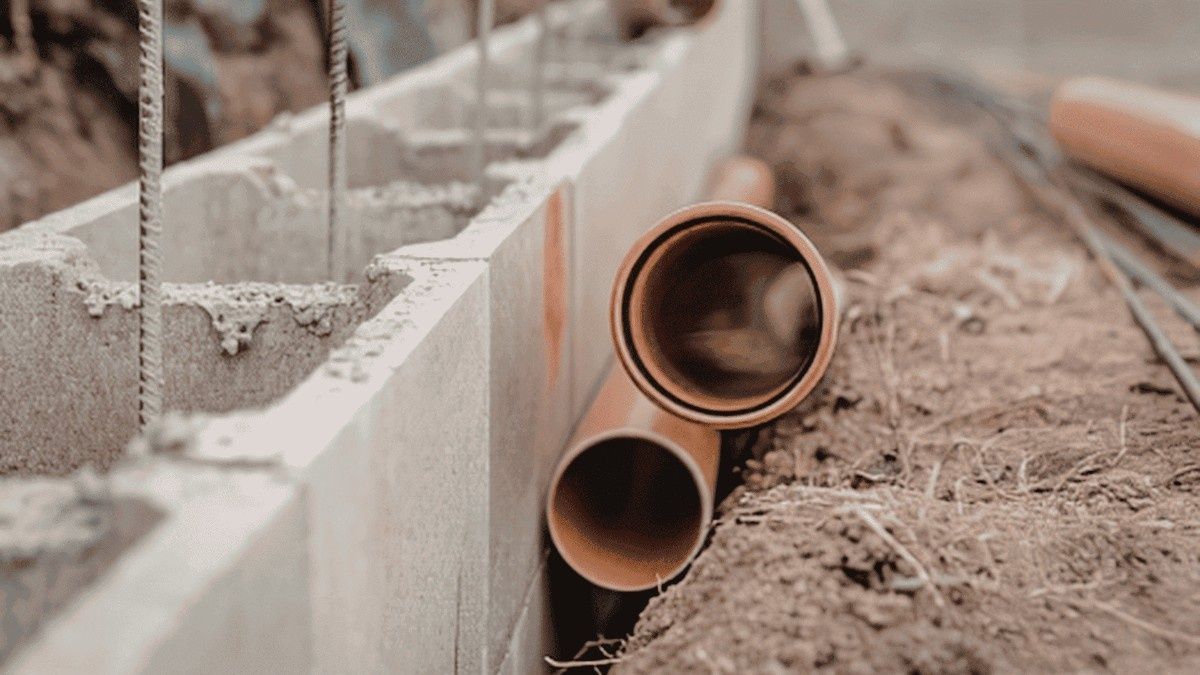 Concrete block wall with two copper pipes protruding from sandy ground at a construction site