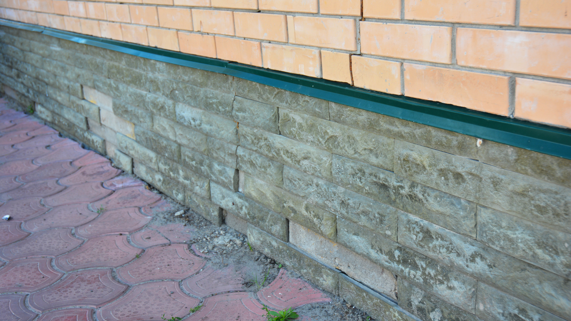 Brick and stone exterior wall beside a paved walkway