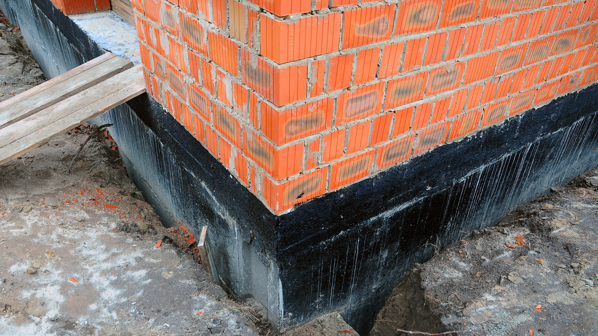 Brick building corner with black waterproofing at the base, seen on a concrete ground.