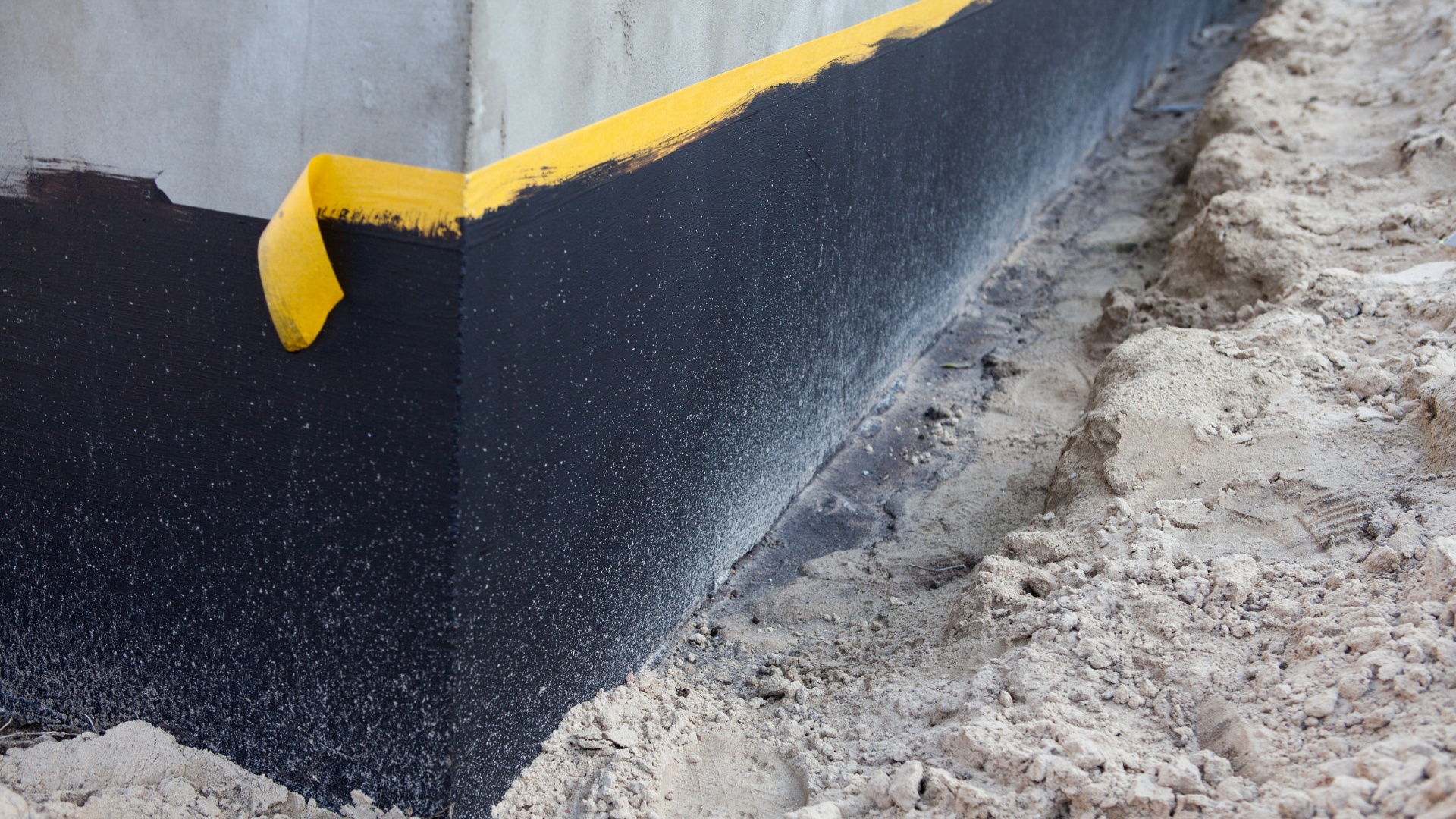 Black-and-yellow curb edge with fresh asphalt beside a concrete and dirt roadside surface