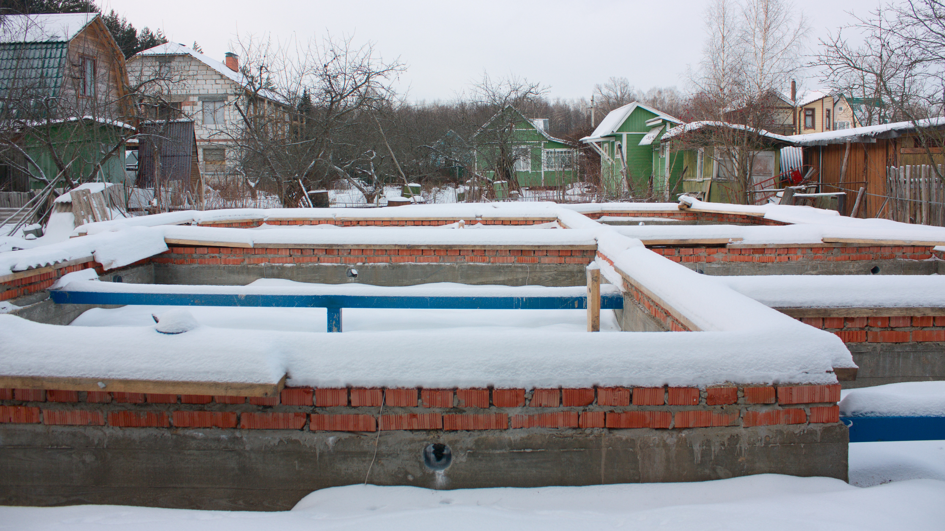 Snow-covered brick pools in a backyard garden with houses and trees in the background