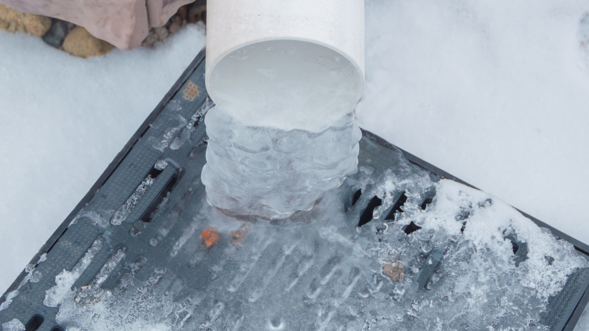 White pipe vent protruding from a snow-covered rooftop with ice buildup around the base
