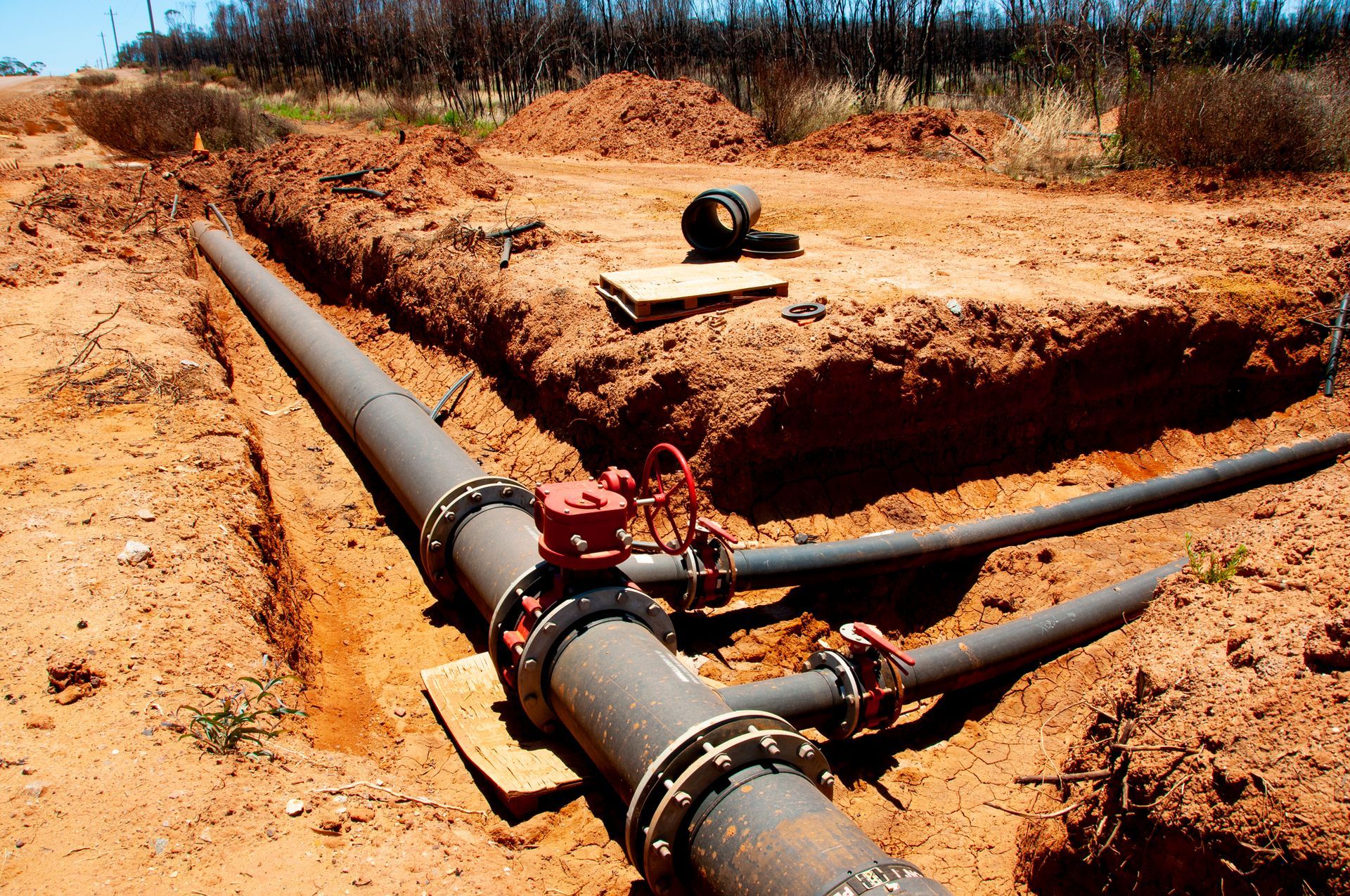 Large pipe in an open trench with a red valve, likely for water or gas distribution.