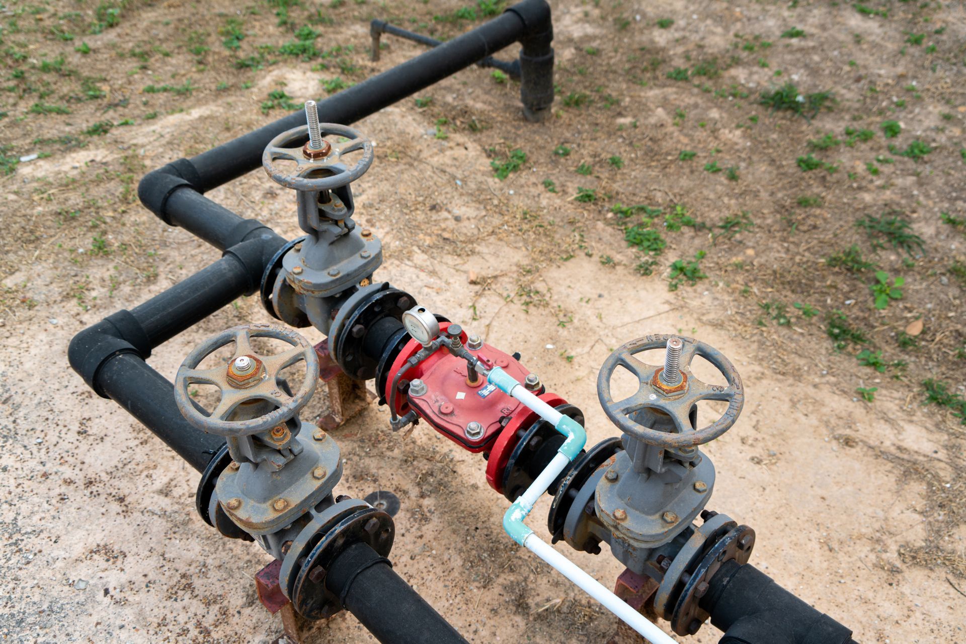 Black pipes with gray valves in a field, red valve in the middle.
