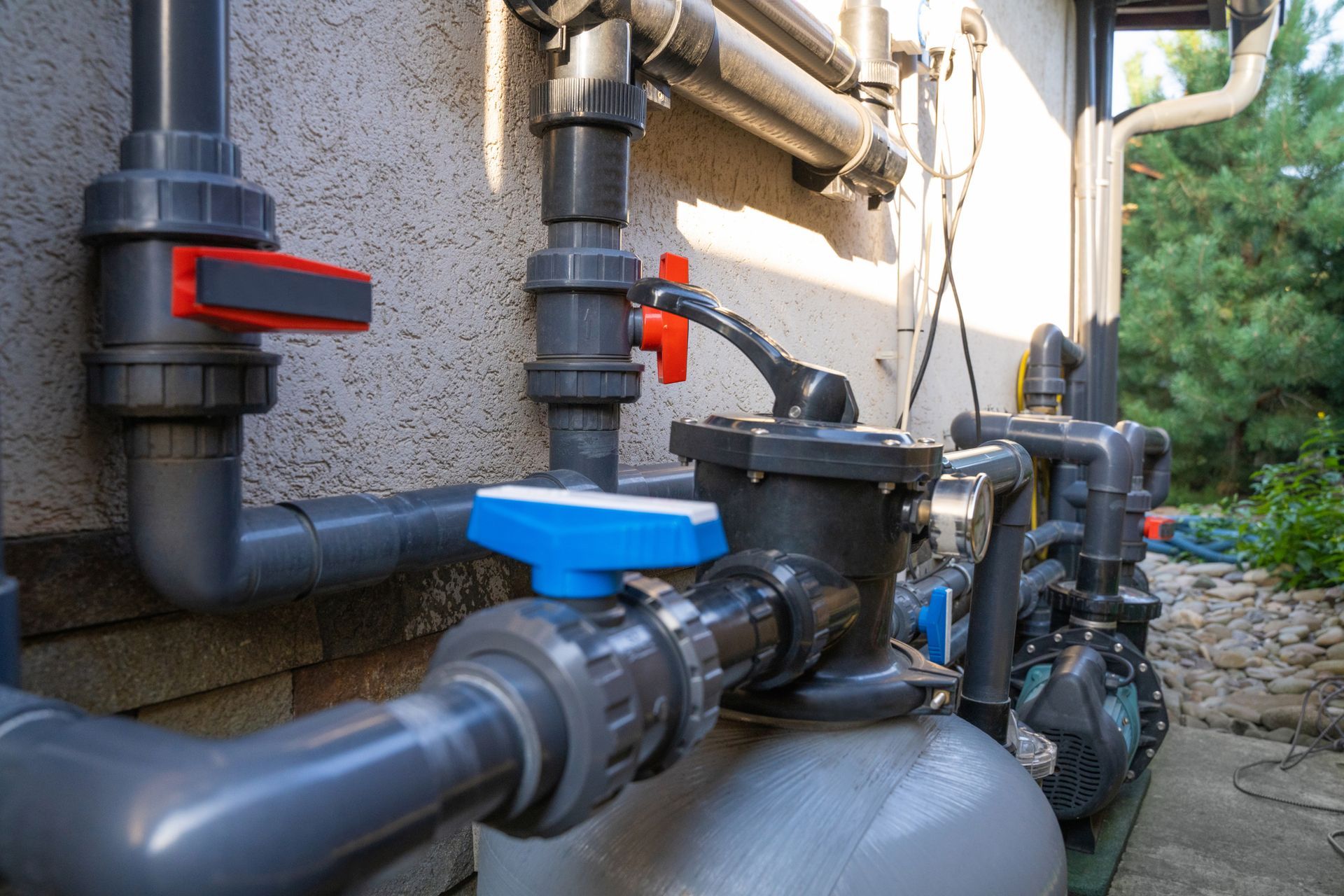 Plumbing system with gray pipes, valves, and filter, mounted on a wall, outdoors.