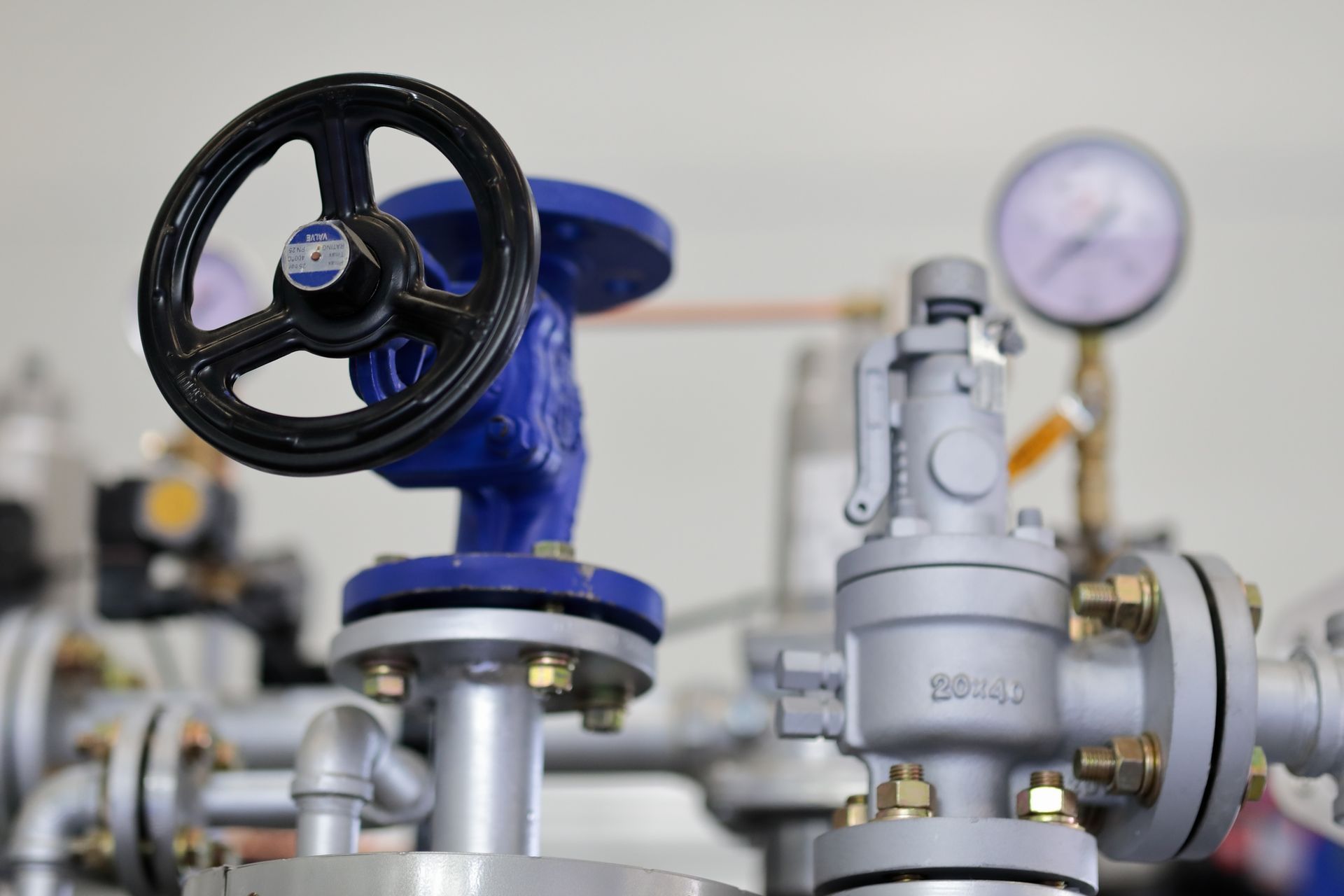 Blue and gray industrial pipes, valve, and gauge with a black handle.