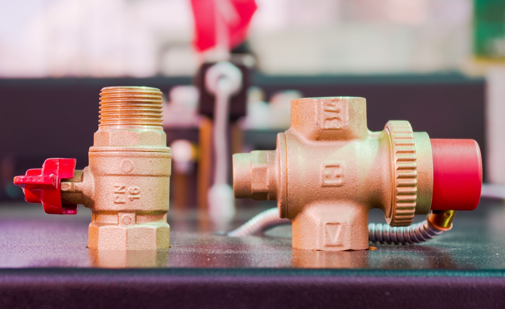 Two brass valves with red handles, one vertical, one horizontal, sit on a dark surface.