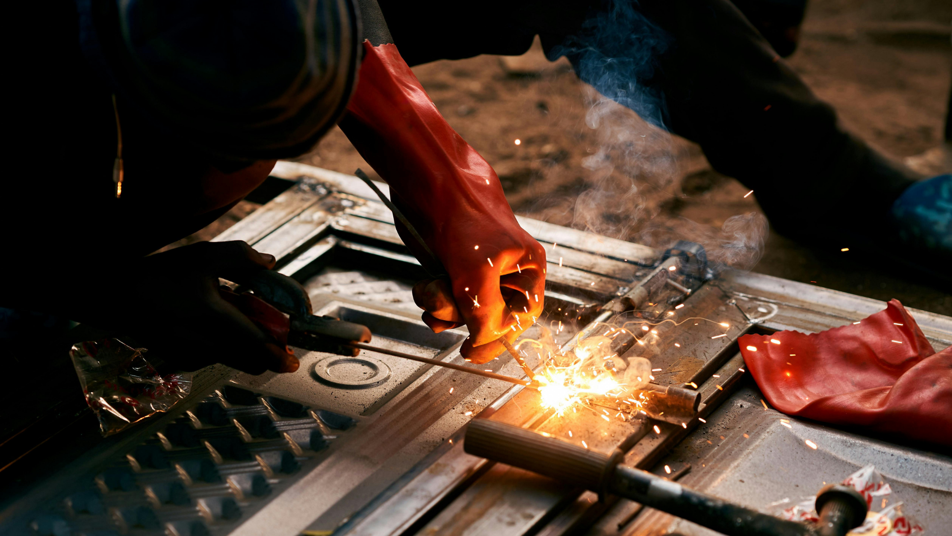 Welder in protective gloves and helmet welding metal with bright blue sparks in a workshop