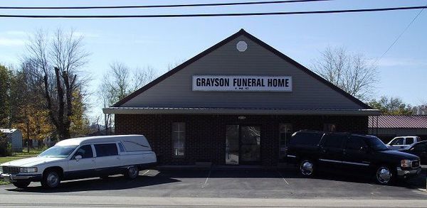 A one-story building with a covered entrance, a blank sign, and an American flag in front against a blue sky.