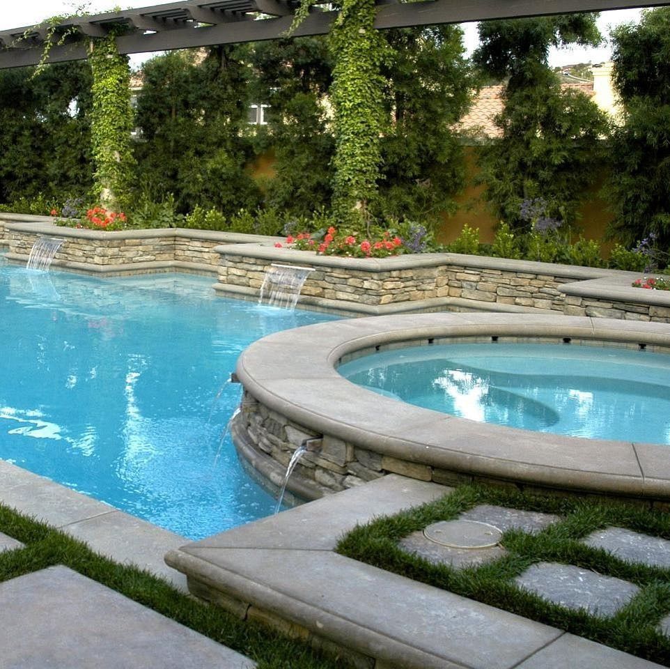 Backyard pool with stone hot tub, blue water, and lush green landscaping