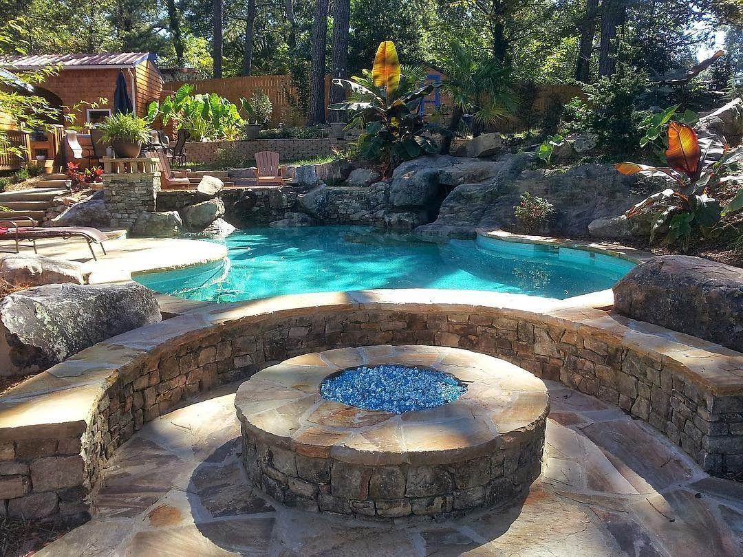 Stone fire pit and turquoise backyard pool surrounded by rocks and trees in a landscaped garden