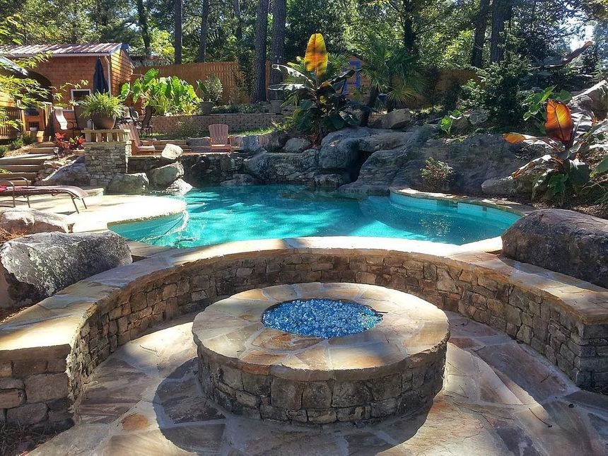 Stone fire pit and turquoise backyard pool surrounded by rocks and trees in a landscaped garden