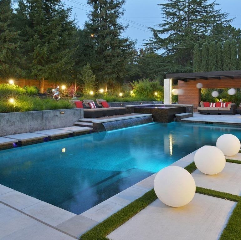 Modern backyard pool at dusk with lounge seating, glowing lights, and white sphere decorations