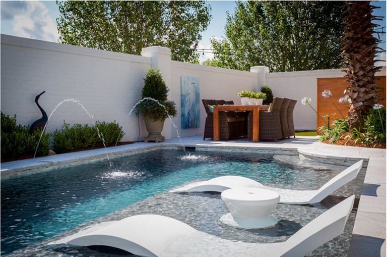 Backyard pool with spa, lounge chairs, and a patio dining area beside a white wall and palm trees