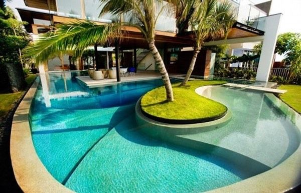 Tropical resort pool with curved turquoise water, palm trees, and a small grassy island centerpiece