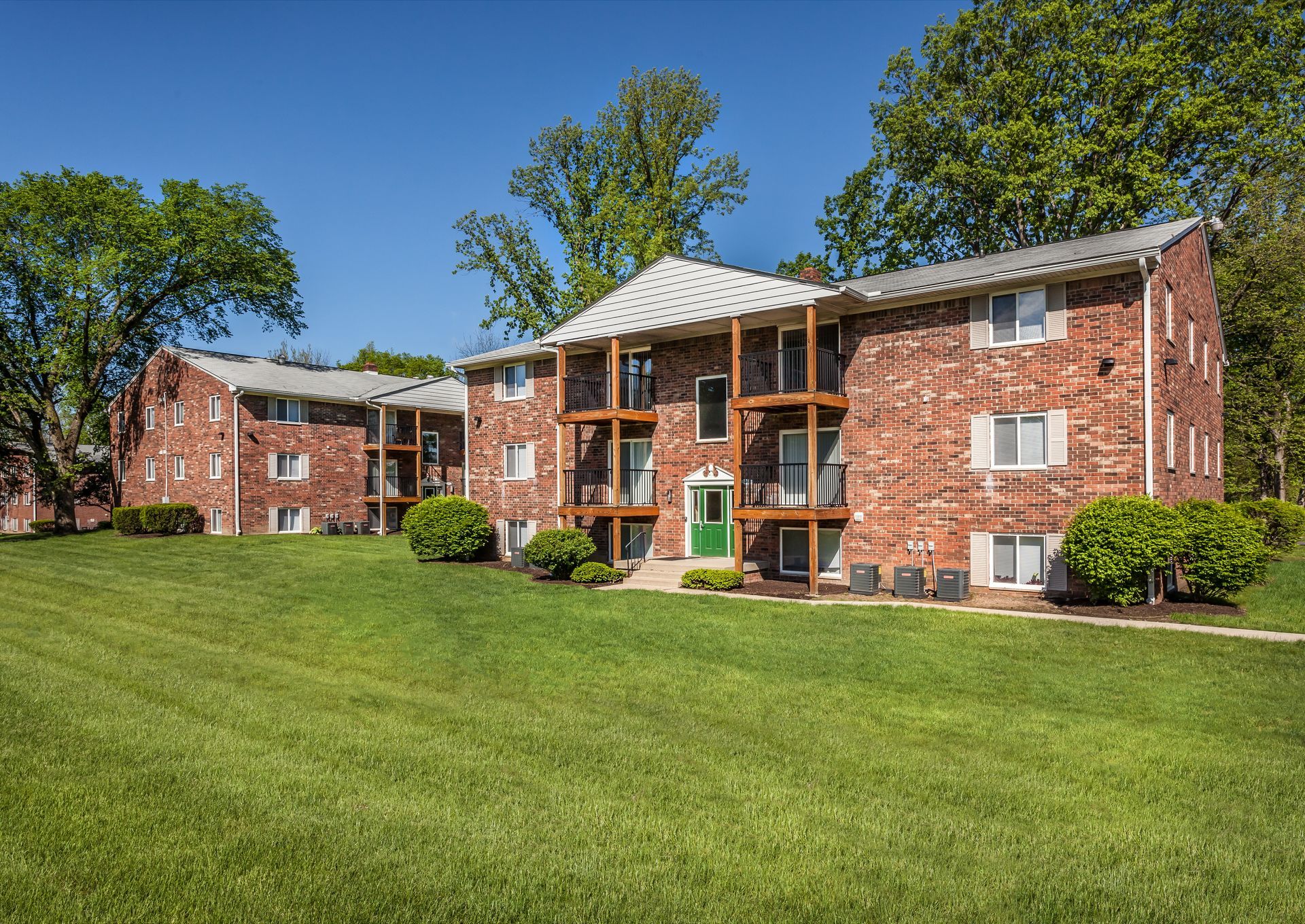A large brick apartment building with a green door is surrounded by lush green grass.