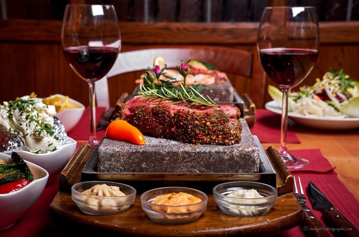 Auf einem Felsen liegt ein Steak mit zwei Gläsern Wein auf einem Tisch.