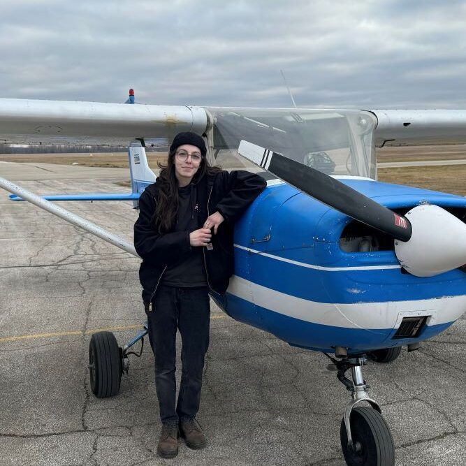 A woman is standing next to a small blue and white plane.
