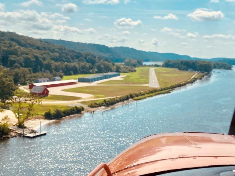 A helicopter is flying over a river with a runway in the background