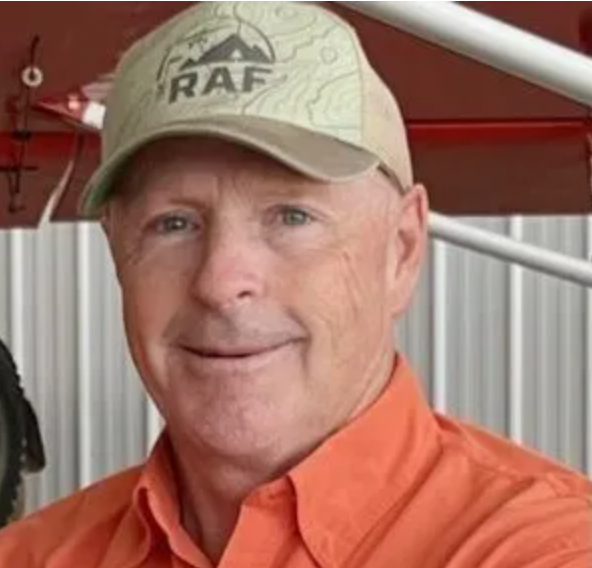 A man in a plaid shirt stands in front of an orange airplane