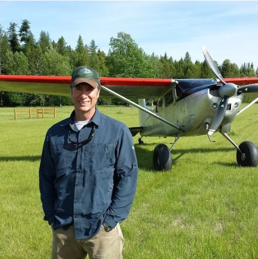 A man wearing a brown leather jacket and a blue shirt is smiling for the camera.