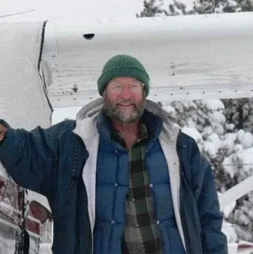Man in plaid shirt and cap, next to a yellow floatplane, holding its wing.