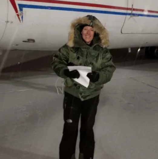 Man in black t-shirt smiles in front of a red and white airplane in a hangar.