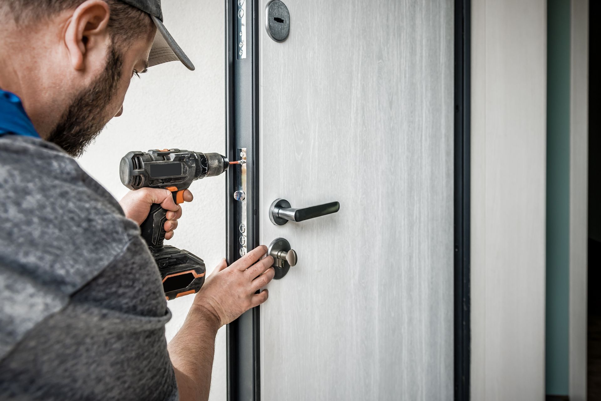 Locksmith repairing residential door lock with cordless drill