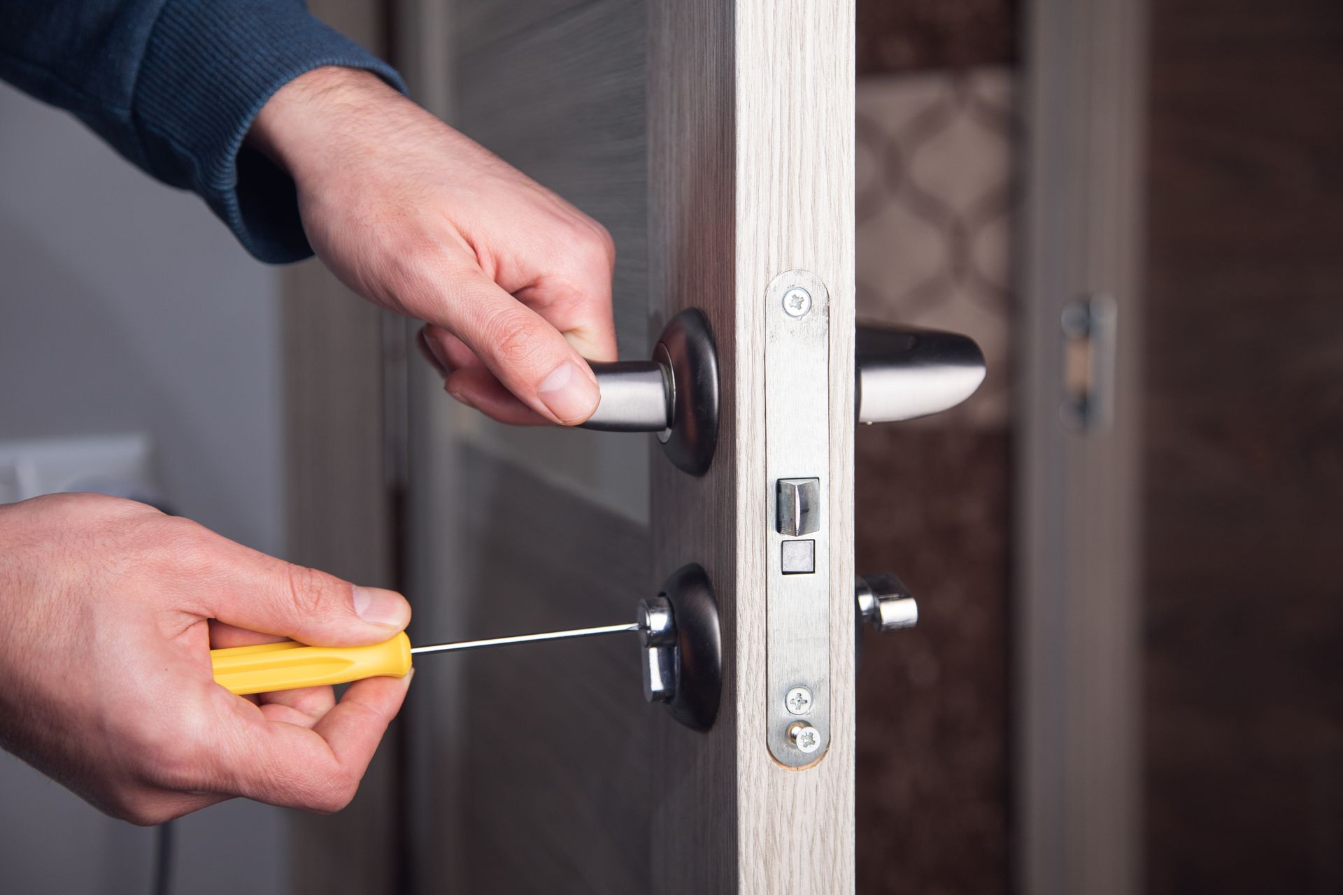 Person using a screwdriver to install or repair a door lock on a light wooden door.