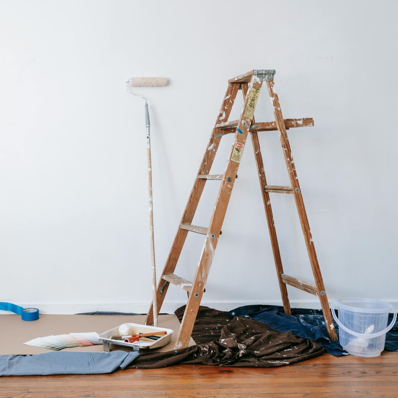 A wooden ladder is leaning against a wall next to a paint roller.