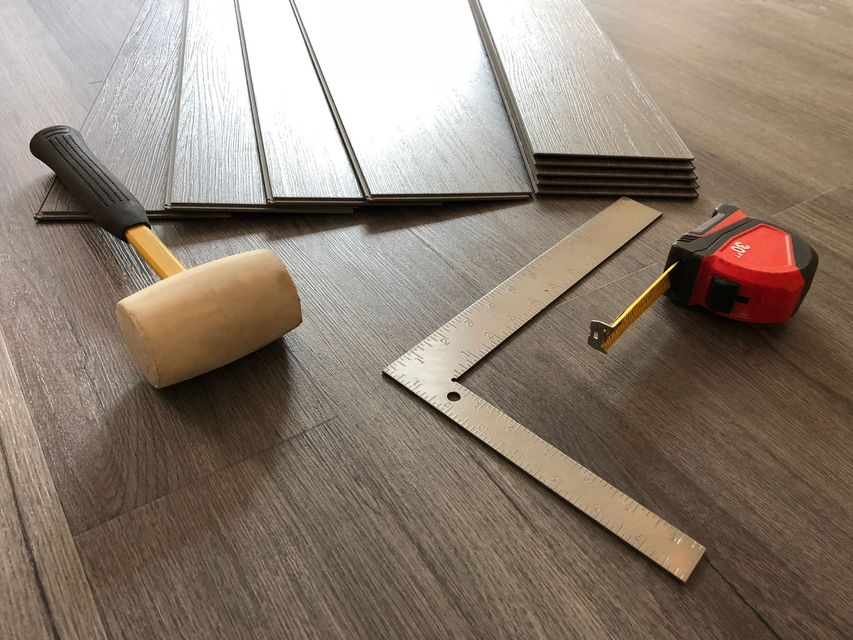 A hammer , ruler , and tape measure are on a wooden floor.